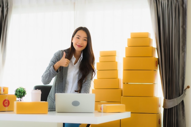 Retrato hermosa mujer de negocios asiática joven trabajar desde casa con teléfono móvil portátil con caja de cartón lista para enviar