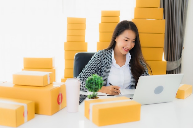 Retrato hermosa mujer de negocios asiática joven trabajar desde casa con teléfono móvil portátil con caja de cartón lista para enviar