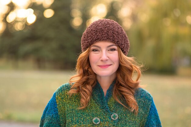 Retrato de una hermosa mujer pelirroja sonriendo en el parque. Feliz señora de mediana edad con sombrero marrón caminando por la naturaleza.