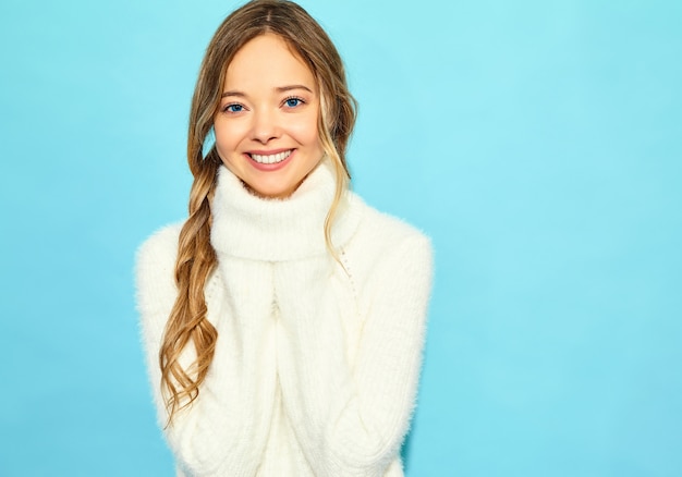 Retrato de hermosa mujer rubia hermosa sonriente. Mujer de pie en el elegante suéter blanco, en la pared azul. Concepto de invierno