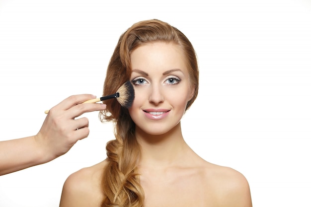 Retrato de hermosa mujer rubia con pelo largo y pincel de maquillaje cerca de cara atractiva