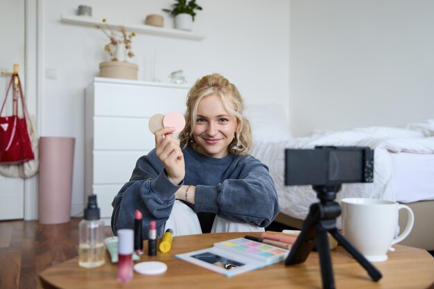 Retrato de una hermosa mujer rubia que muestra productos de belleza ruborizados grabando video en digital