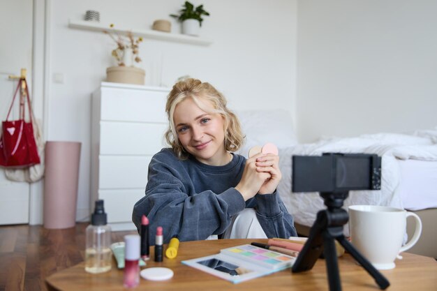 Retrato de una hermosa mujer rubia que muestra productos de belleza ruborizados grabando video en digital