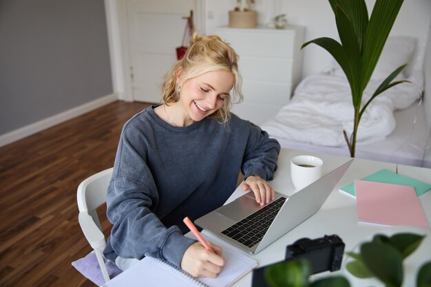 Retrato de una hermosa mujer rubia sonriente escribiendo notas haciendo tareas estudiando desde casa haciendo
