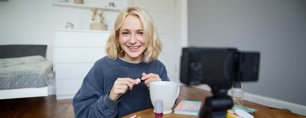 Foto gratuita retrato de una hermosa mujer rubia sonriente grabando un video de su tutorial de maquillaje para social