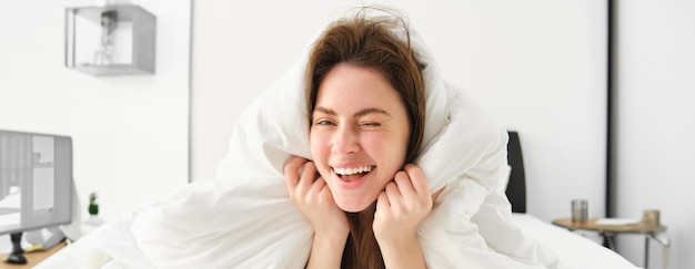 Foto gratuita retrato de una hermosa mujer sonriente acostada en la cama cubierta de edredón tiene el cabello desordenado y parece feliz