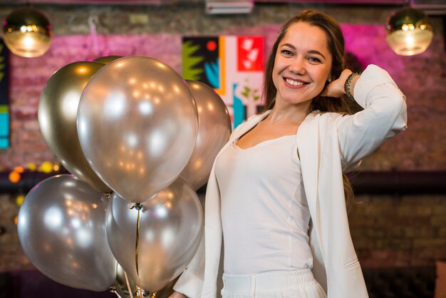 Retrato de una hermosa mujer sonriente posando además de globos de plata