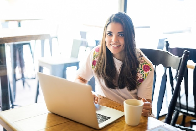 Retrato de una hermosa mujer sonriente sentada en un café con una laptop y una taza de café
