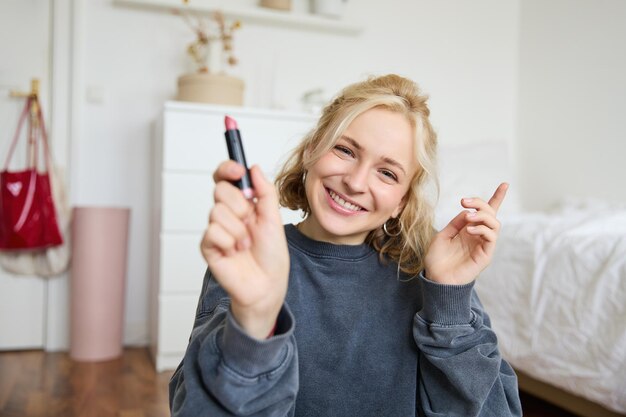 Retrato de una hermosa mujer sonriente en su habitación sentada y mostrando lápiz labial recomendando su favorito