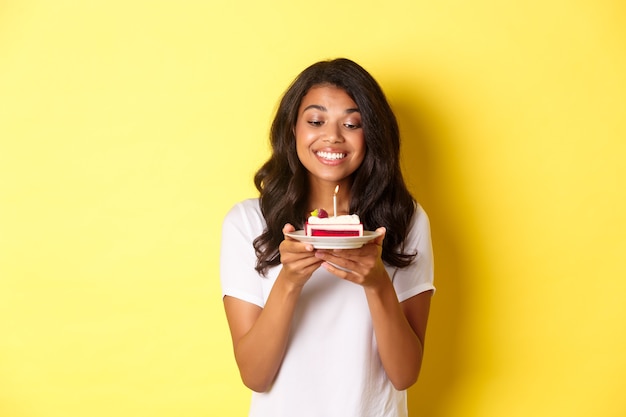 Retrato de hermosa niña afroamericana celebrando un cumpleaños sonriendo y mirando feliz en el pastel de cumpleaños