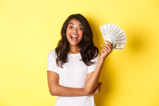 Retrato de hermosa niña afroamericana sonriendo feliz y mostrando dinero yendo de compras de pie