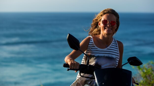 Retrato de una hermosa niña conduciendo un scooter en un acantilado con una increíble vista al mar.