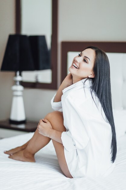 Retrato de una hermosa niña morena feliz sentada en la cama y posando.