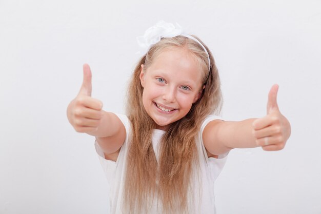 Retrato de una hermosa niña mostrando los pulgares para arriba en blanco