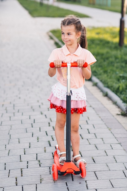 Foto gratuita retrato de una hermosa niña de pie en patinete scooter en el parque