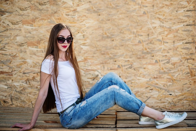 Retrato de una hermosa niña sentada sobre tablas de madera contra la pared de chapa