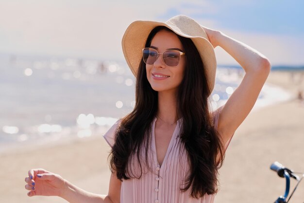 Retrato de una hermosa niña sonriente con gafas de sol y vestido rosa en la tranquila playa.