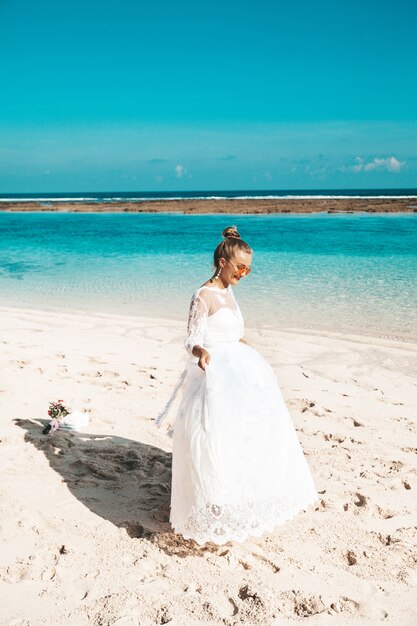 Retrato de la hermosa novia bailando en la playa detrás del cielo azul y el mar
