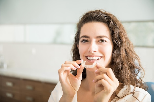 Retrato de hermosa paciente sosteniendo retenedores de ortodoncia en clínica dental