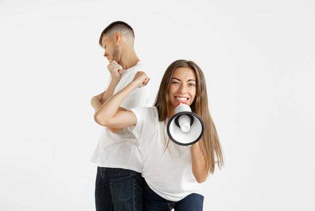 Retrato de hermosa pareja joven aislado sobre fondo blanco de estudio. Expresión facial, emociones humanas, concepto publicitario. Mujer gritando en paz, loca y feliz. El hombre es indiferente.