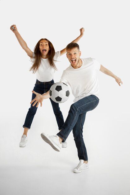 Retrato de hermosa pareja joven aislado sobre fondo blanco de estudio. Expresión facial, emociones humanas, publicidad, apuestas, concepto deportivo. Hombre y mujer jugando al fútbol o al fútbol en acción.