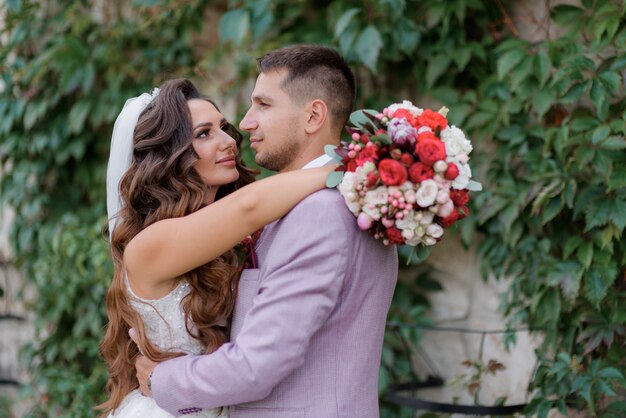 Retrato de una hermosa pareja de novios delante de una pared cubierta de hojas verdes