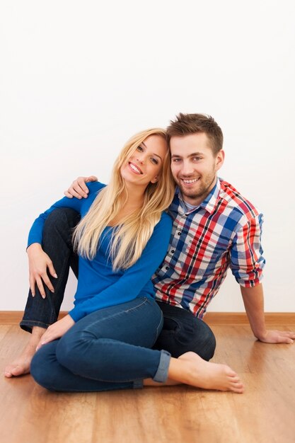 Retrato de hermosa pareja sentada en el piso de madera en casa