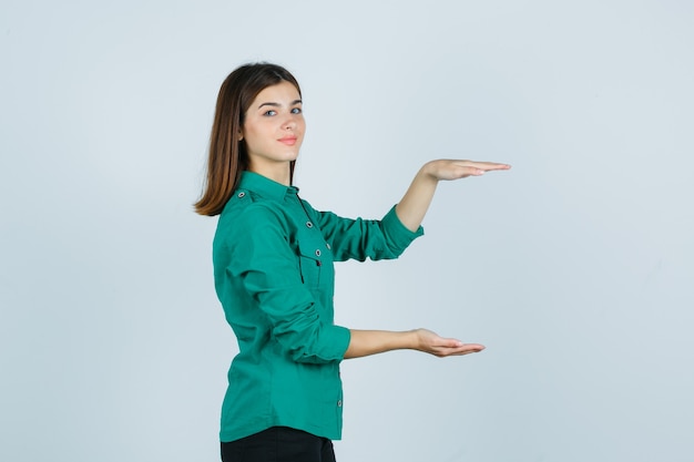 Foto gratuita retrato de hermosa señorita mostrando cartel de gran tamaño en camisa verde y mirando alegre