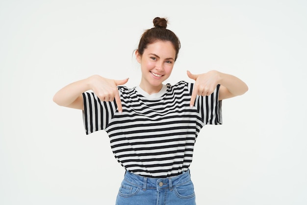 Foto gratuita retrato de una hermosa y sonriente joven modelo femenina que muestra un anuncio apuntando con los dedos hacia abajo