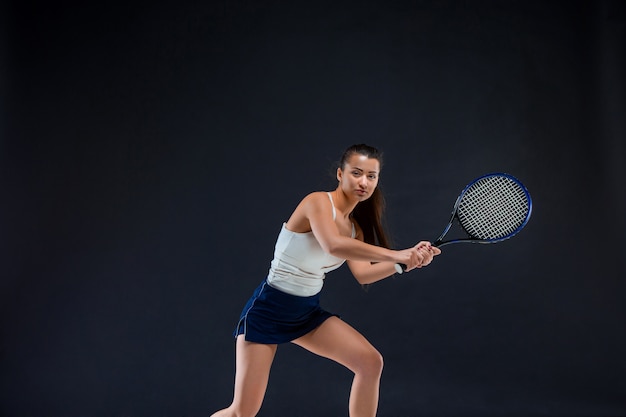 Retrato de la hermosa tenista con una raqueta en la pared oscura
