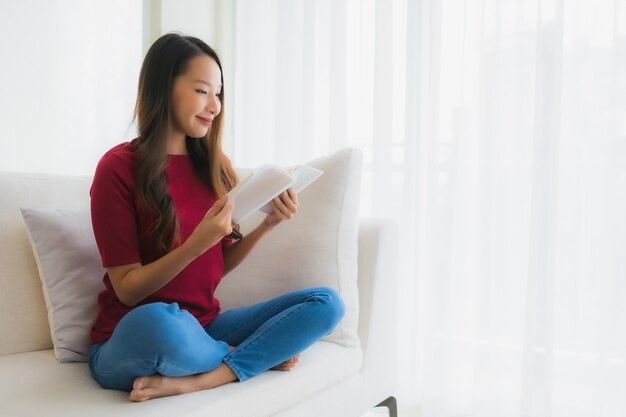 Retrato hermosas mujeres asiáticas jóvenes leen el libro en la silla del sofá