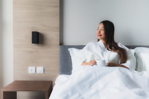 Retrato hermosas mujeres asiáticas jóvenes con taza de café en la cama