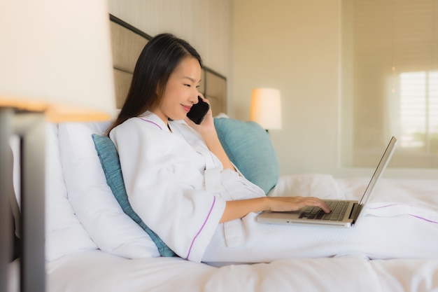 Retrato hermosas mujeres asiáticas jóvenes usando una computadora portátil o computadora con el móvil en la cama