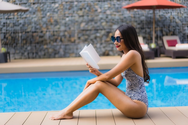 Retrato hermosas mujeres asiáticas leen el libro alrededor de la piscina al aire libre