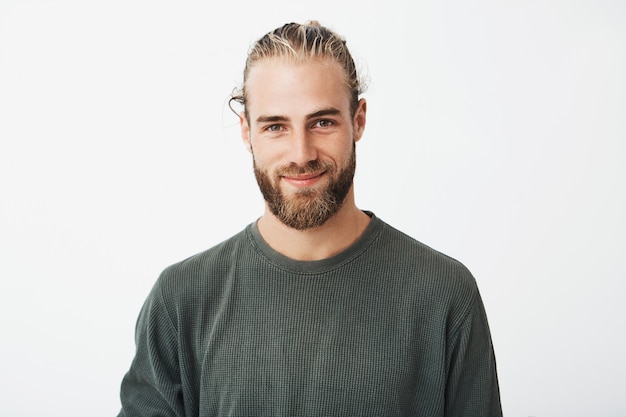 Retrato de un hermoso chico barbudo rubio maduro con peinado de moda en camisa gris informal sonriendo