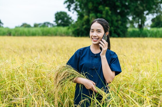 Retrato hermoso joven agricultor asiático usa smartphone en campo de arroz orgánico y sonríe con felicidad