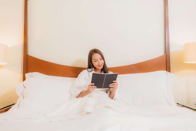 Retrato hermoso libro de lectura de la mujer asiática joven en la cama en el interior del dormitorio