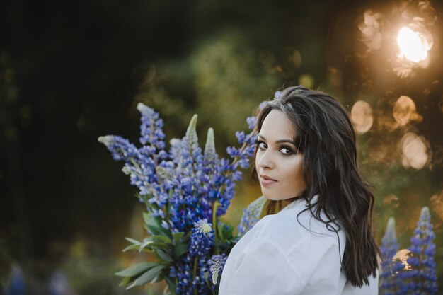 Retrato hermoso de la mujer con el ramo de lupinus en puesta del sol