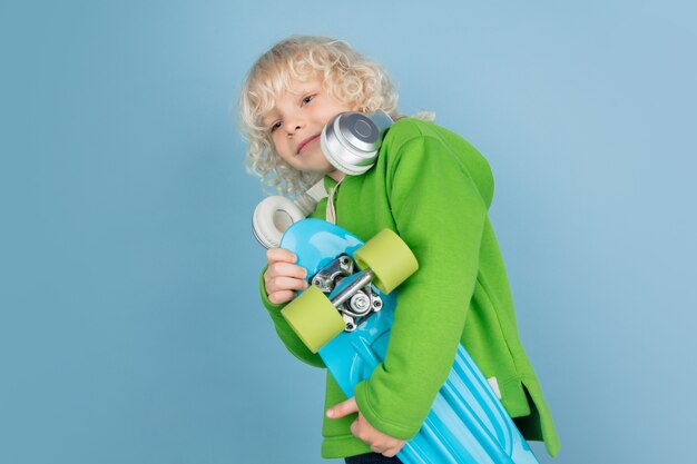 Retrato de hermoso niño caucásico aislado sobre fondo azul de estudio. Modelo masculino rubio rizado. Concepto de expresión facial, emociones humanas, infancia, publicidad, ventas.