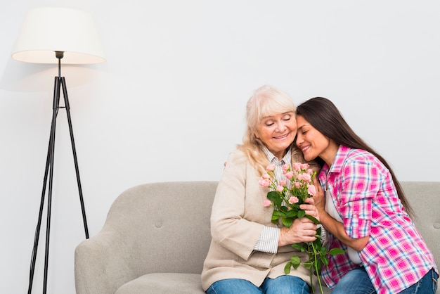 Foto gratuita retrato de la hija adulta sonriente que abraza a su madre mayor feliz que sostiene el ramo de la flor