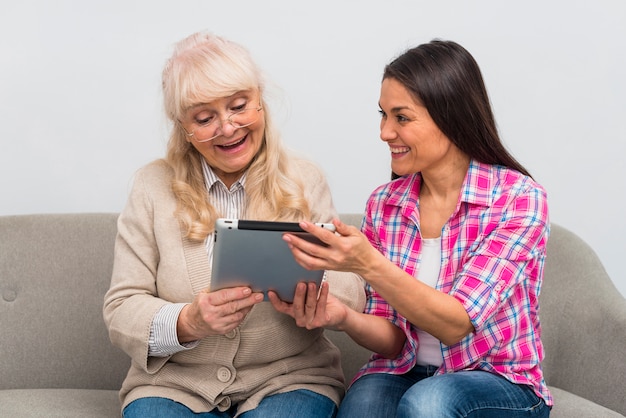 Retrato de hija alegre mostrando tableta digital a su madre senior