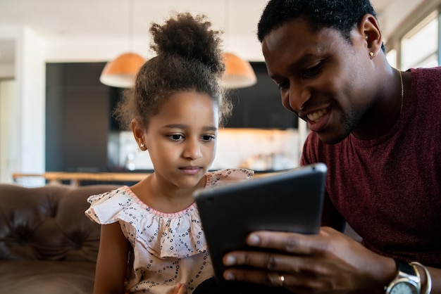 Retrato de una hija y un padre divirtiéndose juntos y jugando con tableta digital en casa