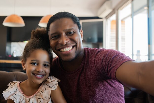 Retrato de una hija y un padre divirtiéndose juntos y tomando un selfie mientras está sentado en el sofá en casa