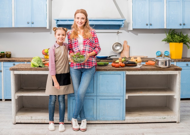 Retrato de una hija sonriente de pie con su madre sosteniendo un tazón de ensalada