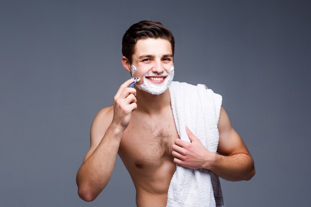 Retrato de hombre afeitado guapo sonriente en el tiempo de la mañana, aislado en la pared gris