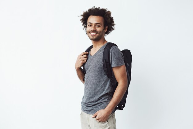 Retrato de hombre africano alegre con mochila sonriendo listo para ir en un largo viaje de senderismo o luchar por la educación