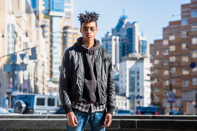 Retrato del hombre africano joven elegante que se opone a horizonte de la ciudad