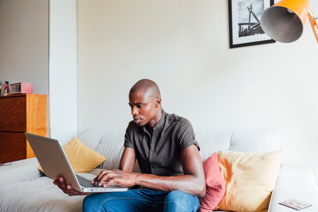 Retrato de un hombre africano joven que usa el ordenador portátil en casa