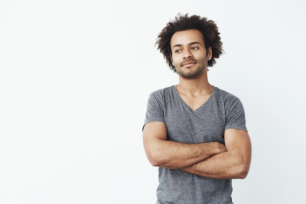 Foto gratuita retrato del hombre africano stong y hermoso que mira a la izquierda que presenta con los brazos cruzados sobre la pared blanca. concepto de inicio seguro.