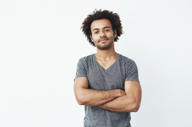 Retrato del hombre africano stong y hermoso que presenta con los brazos cruzados sobre el fondo blanco. Emprendedor o estudiante seguro.